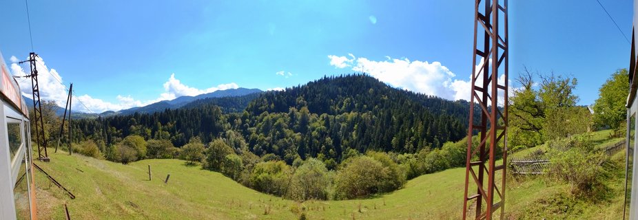 Panoramic view of forest-covered mountains and green meadows in Borjomi, Georgia, with blue sky and white clouds above