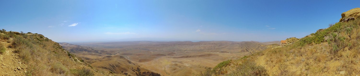 Wide panoramic landscape showing a vast valley with golden-brown hills under a clear blue sky, viewed from an elevated position in Signagi, Georgia