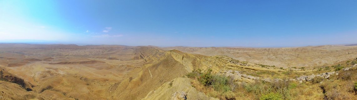 Panoramic landscape showing golden-brown arid hills and valleys under a clear blue sky near Signagi, Georgia