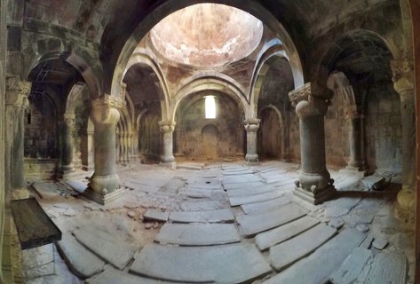 Interior view of medieval stone monastery with columns, arches, and central dome with light streaming through opening above