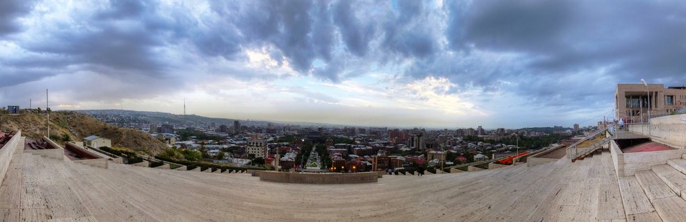 Wide panoramic cityscape of Yerevan Armenia viewed from elevated stone terrace steps with dramatic cloudy sky above urban buildings