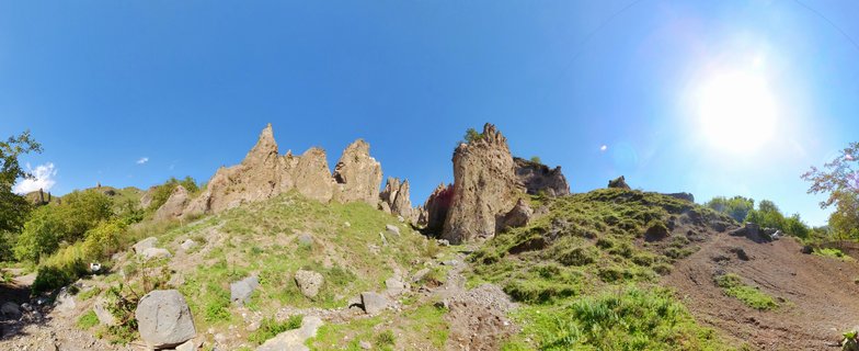 Panoramic view of eroded rock formations on grassy hills under bright blue sky with visible sun in Goris, Armenia