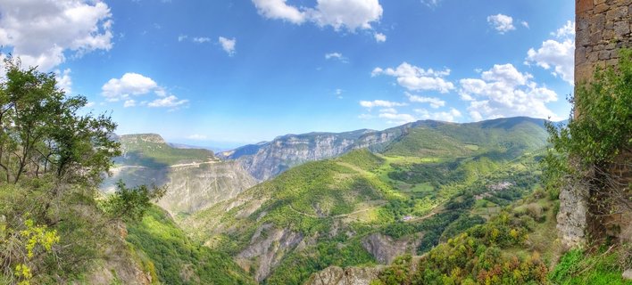 Panoramic landscape showing green mountain valleys and the Vorotan Gorge near Tatev Monastery in Armenia, with blue sky and white clouds above
