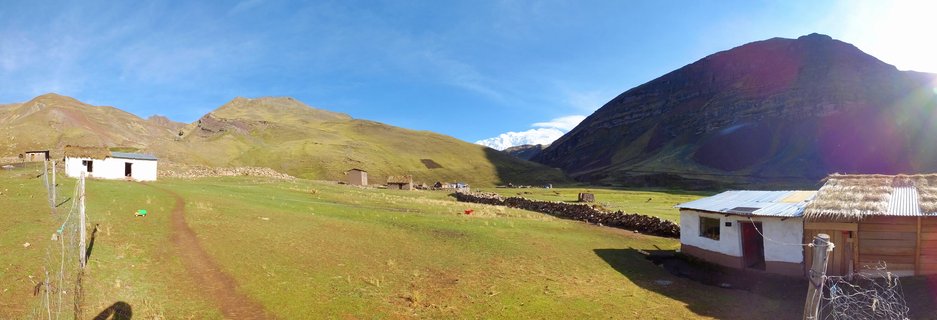 White rural houses with metal and thatched roofs in a green mountain valley with colorful stratified mountain slopes under blue sky in Peru