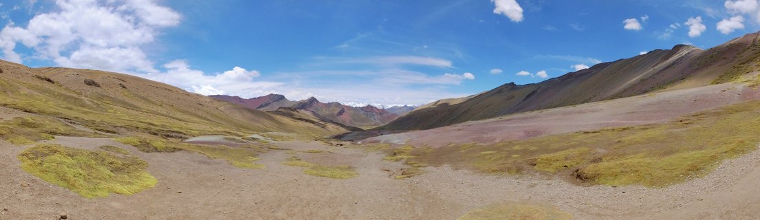 Wide valley landscape with colorful stratified mountains in the distance under blue sky with white clouds, Rainbow Mountain region Peru