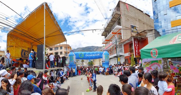 Crowd of people at a street festival in Andahuaylas, Peru, with a yellow stage, blue inflatable arch, and mountains in the background
