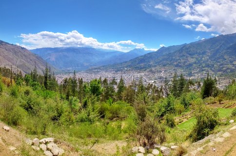 Wide panoramic view of Andahuaylas city in a valley surrounded by green and brown mountains under blue sky with white clouds, Peru