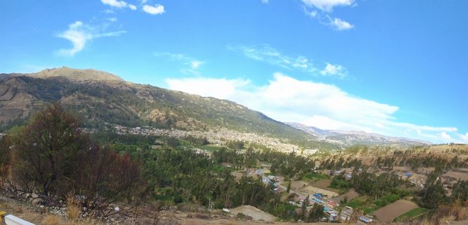 Wide panoramic landscape showing a valley city with white buildings surrounded by brown and green mountains under a blue sky with white clouds in Ayacucho, Peru