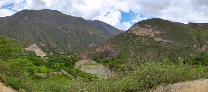 Wide mountain valley in Peru with a winding river, green slopes, and cloudy sky