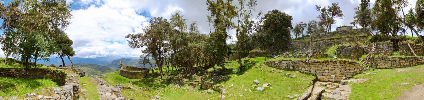Ancient stone fortress ruins with circular walls and terraces on a green mountain ridge under partly cloudy sky in Peru
