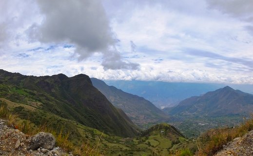 Mountain valley landscape showing green Andean slopes descending into a wide valley with scattered settlements, under a cloudy sky in Cajamarca, Peru