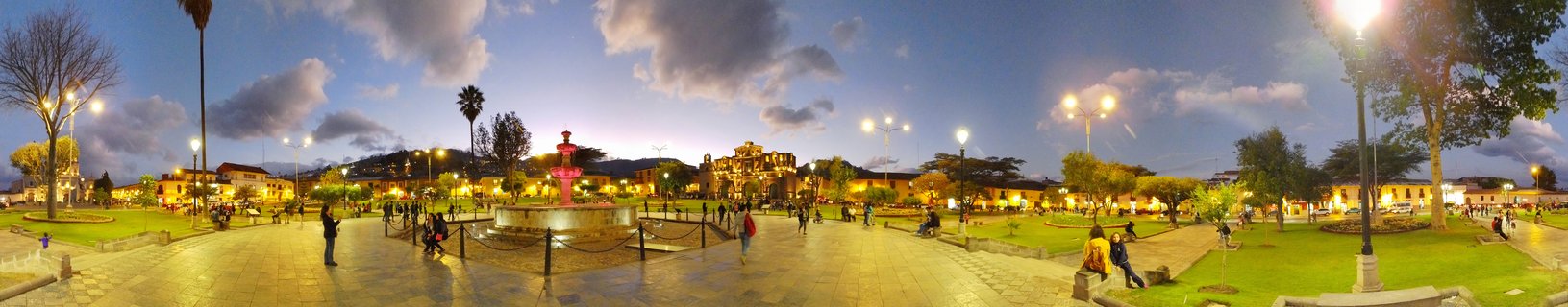 Cajamarca's Plaza de Armas at blue hour features an illuminated pink fountain as the centerpiece, surrounded by colonial buildings, a historic church, and locals enjoying the evening in Peru's northern highlands.