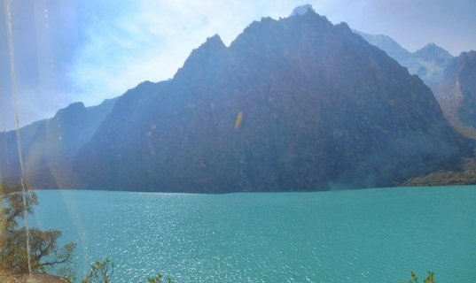Turquoise alpine lake with dark mountain peaks rising in the background under a bright sky in Huaraz, Peru