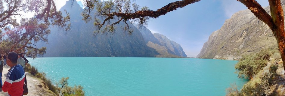 Turquoise glacial lake surrounded by steep mountain walls in the Peruvian Andes, with a tree branch framing the top of the scene