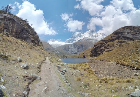 Mountain hiking trail leading to an alpine lake with snow-covered peaks in the Peruvian Andes near Huaraz