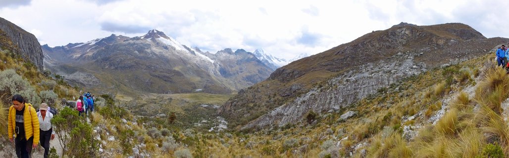 Group of hikers with backpacks walking on mountain trail with snow-capped Andes peaks and valley landscape in background