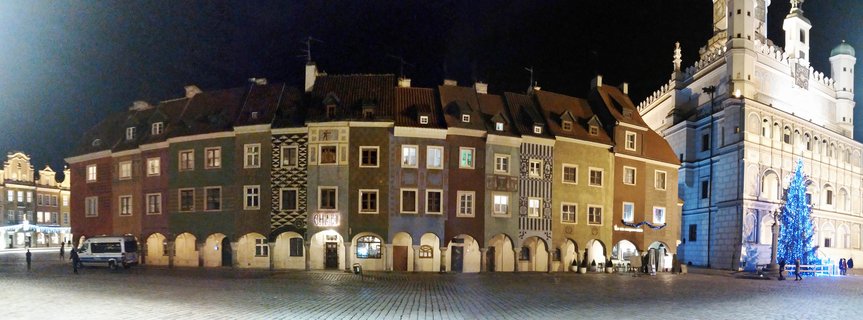 Night view of colorful historic buildings and illuminated white Town Hall in Poznan's Old Market Square with cobblestone plaza and Christmas tree