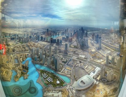 High-angle view of Dubai Marina showing skyscrapers along a turquoise artificial waterway with roads and construction areas visible throughout the urban landscape