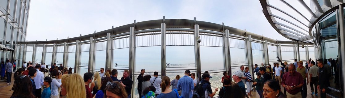 Crowd of tourists on Burj Khalifa observation deck with curved metal safety railings overlooking Dubai cityscape