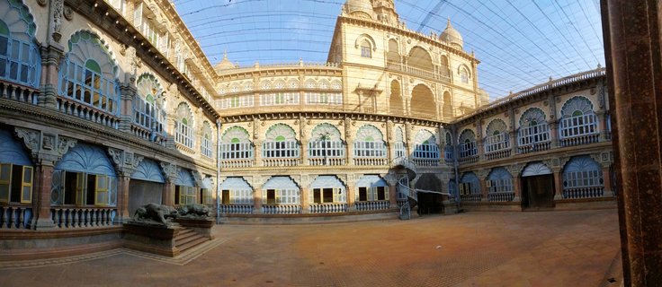Interior courtyard of Mysore Palace showing three-story ornate building with arched windows, balconies, stone sculptures, and paved courtyard under protective netting