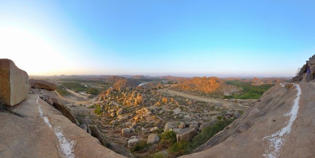 Panoramic landscape view of Hampi's granite boulder field with ancient temple ruins, captured from elevated rocky viewpoint during golden hour with clear blue sky