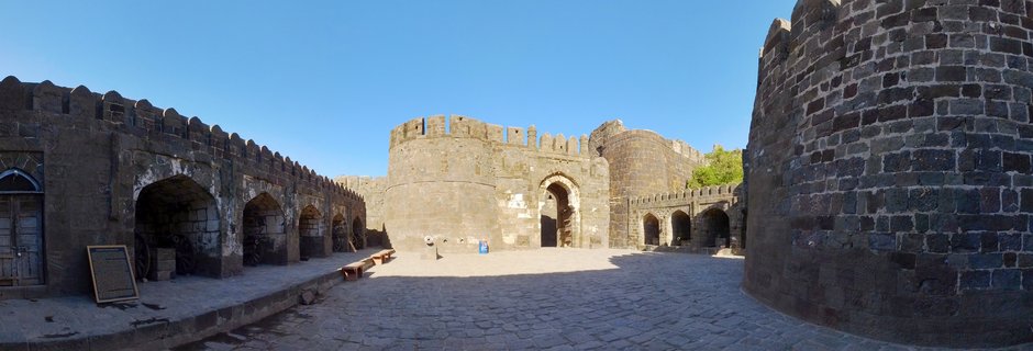 Stone courtyard of medieval Indian fort with crenellated walls, arched doorways, and cannons under blue sky