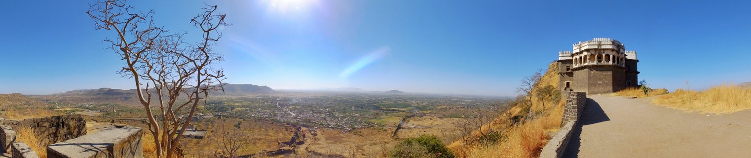 Historic stone fort structure on hilltop overlooking vast valley with dry golden grasslands, distant mountains, and clear blue sky in Aurangabad, India