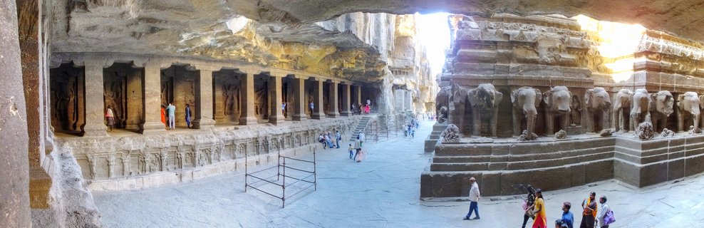 Rock-cut temple complex at Ellora Caves showing elephant sculptures, stone pillars, and visitors exploring the ancient monument