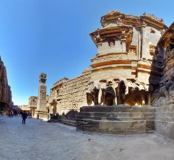 Kailasa Temple at Ellora Caves showing monolithic rock-cut Hindu temple with carved elephant sculptures at base, stone pillars, intricate friezes, and tourists in courtyard under clear blue sky