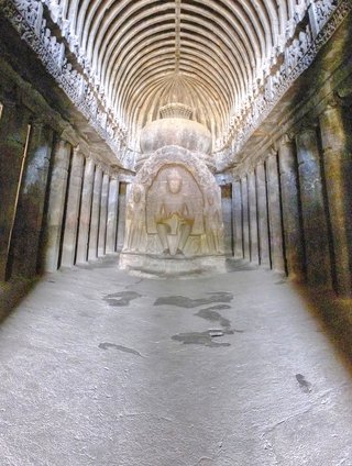 Interior view of ancient Buddhist cave temple with central stupa sculpture, carved pillars lining both sides, and ribbed arched ceiling