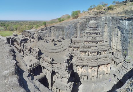 Aerial view of the Kailasa Temple carved into a rock cliff at Ellora Caves with courtyard, sculptures, and surrounding landscape under clear blue sky