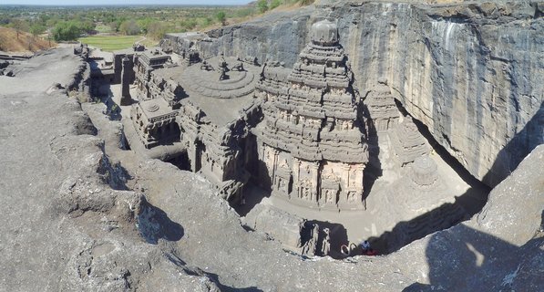 Elevated view of the Kailasa Temple carved from dark basalt rock at Ellora Caves with visitors visible for scale and dry landscape beyond