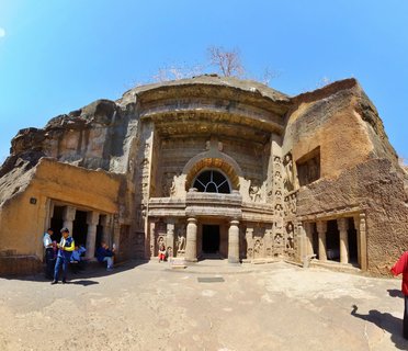 Ornate facade of ancient Buddhist Cave 19 carved into rock cliff with columns, sculptures, and arched window under clear blue sky at Ajanta Caves, India