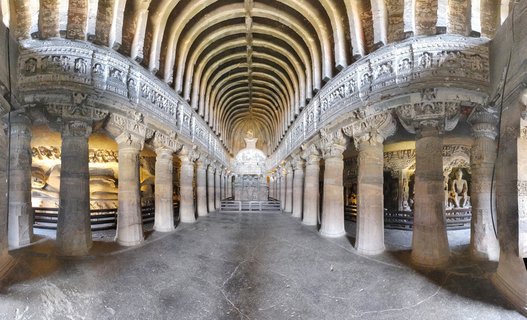 Interior view of ancient rock-cut Buddhist cave temple with rows of carved stone pillars, vaulted ribbed ceiling, and stupa monument at the far end