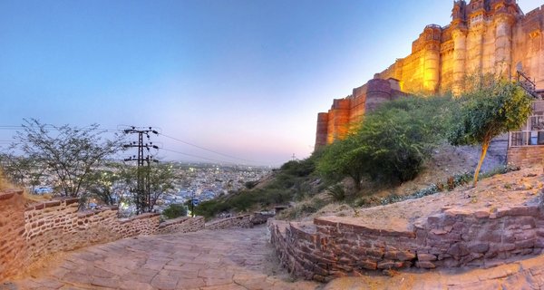 Illuminated Mehrangarh Fort on a hilltop at twilight with Jodhpur's blue city visible in the valley below