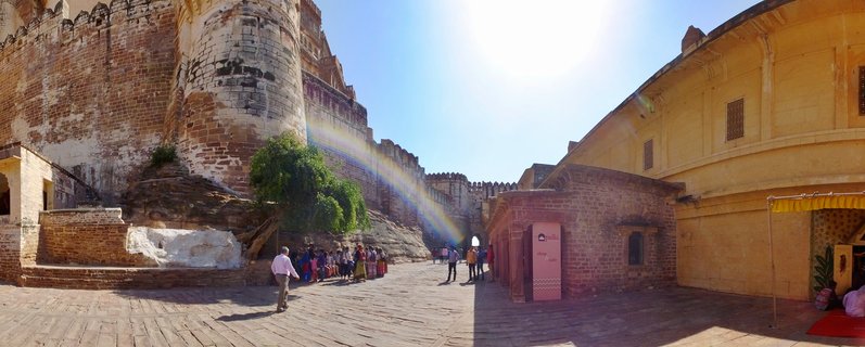 Wide courtyard of Jaisalmer Fort showing golden sandstone walls, bastions, and visitors walking on stone pavement under bright sunlight with clear blue sky