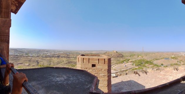 Panoramic view from a sandstone fort bastion showing historic cannons, fortification walls, and the city of Jaisalmer in the desert landscape of Rajasthan, India
