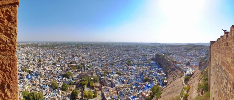Panoramic view of densely packed blue-painted buildings in Jaisalmer city from elevated fort position with sandstone walls framing the scene