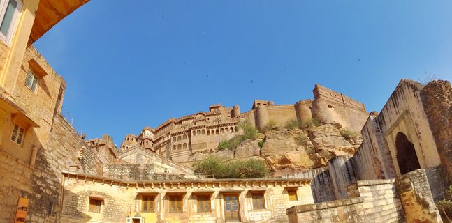 Jaisalmer Fort built from golden sandstone sits atop a rocky hill with traditional Rajasthani buildings in the foreground under a clear blue sky