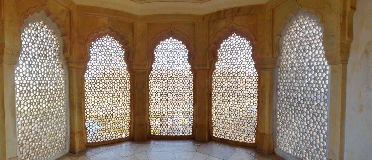 Interior view of five arched windows with white honeycomb lattice stone screens set in golden sandstone walls at Amber Fort, Jaipur
