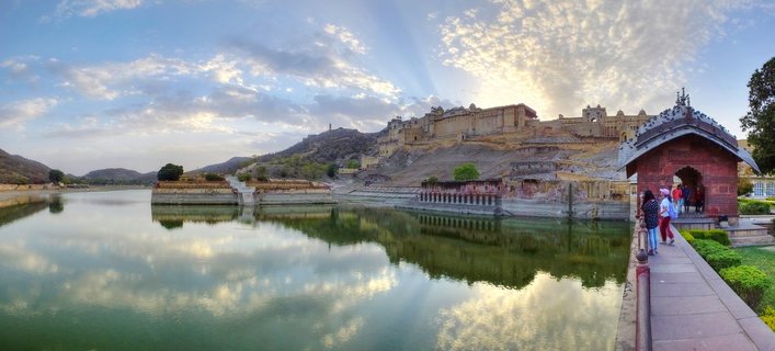Amber Fort palace complex on hillside with reflection in Maota Lake, visitors at pavilion, Jaipur, India