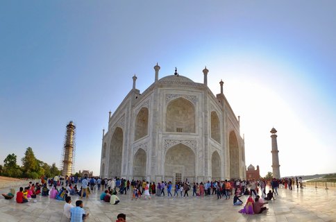White marble Taj Mahal mausoleum with four minarets and crowds of tourists on the plaza under clear blue sky in Agra, India