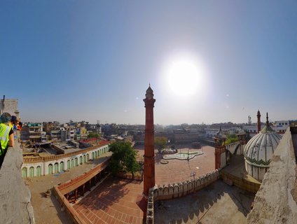 Elevated panoramic view of Jama Masjid mosque showing red sandstone minaret, white domes, courtyard with visitors, and Old Delhi cityscape under bright morning sun