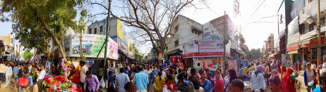 Busy street market in Delhi with crowds of people shopping, colorful storefronts, Hindi signage, and vendors selling goods under bright daylight