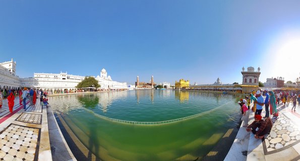 Panoramic view of the Golden Temple (Harmandir Sahib) in Amritsar, India, showing the golden shrine surrounded by a sacred pool with pilgrims walking along white marble walkways under a clear blue sky