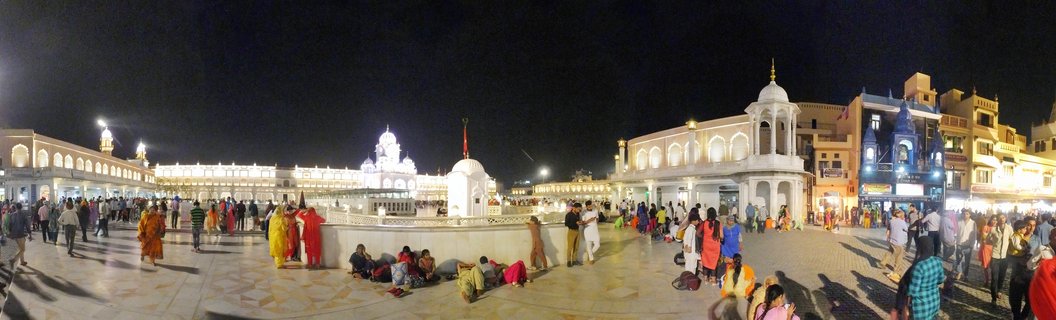 Night view of the illuminated Golden Temple complex in Amritsar with visitors in colorful clothing walking across the marble courtyard