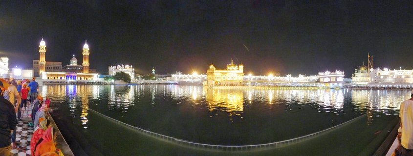 Night photograph of the Golden Temple in Amritsar India showing the golden illuminated sanctuary reflected in the sacred pool with visitors walking along the marble pathway
