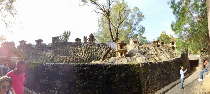 Miniature stone temple structures built into terraced rock formations at Rock Garden Chandigarh with visitors walking on cobblestone paths