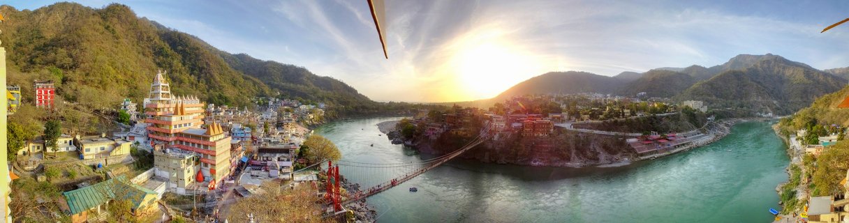Panoramic view of suspension bridge over turquoise river with Hindu temples and mountains at sunset in Rishikesh India