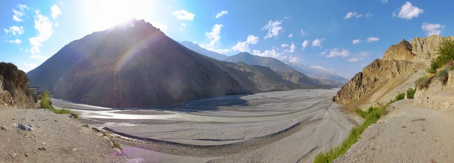 Wide panoramic view of Kali Gandaki River valley with braided water channels flowing between steep arid mountains under a blue sky with scattered clouds near Kagbeni, Nepal